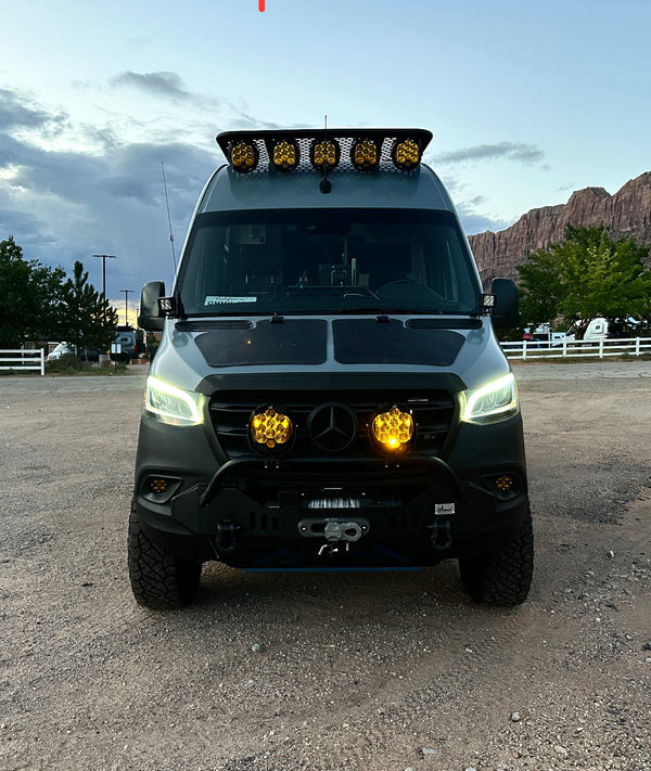 Custom Mercedes Sprinter van displays upgraded off-road features, including a roof rack, LED light bar, and a rugged front bumper. 
