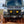 A mud-splattered Mercedes Sprinter van powers through a muddy trail. 
